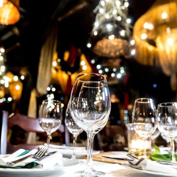 A close-up of empty wine glasses and place settings on a table in a warmly lit, elegant restaurant with decorative lights and a festive atmosphere—perfect for gatherings or celebrating milestones with local insurance agents.