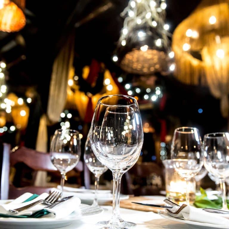 A close-up of empty wine glasses and place settings on a table in a warmly lit, elegant restaurant with decorative lights and a festive atmosphere—perfect for gatherings or celebrating milestones with local insurance agents.